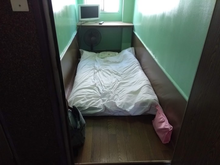 Hotellihuoneeni, jossa oli futon-sänky, tuuletin ja televisio.